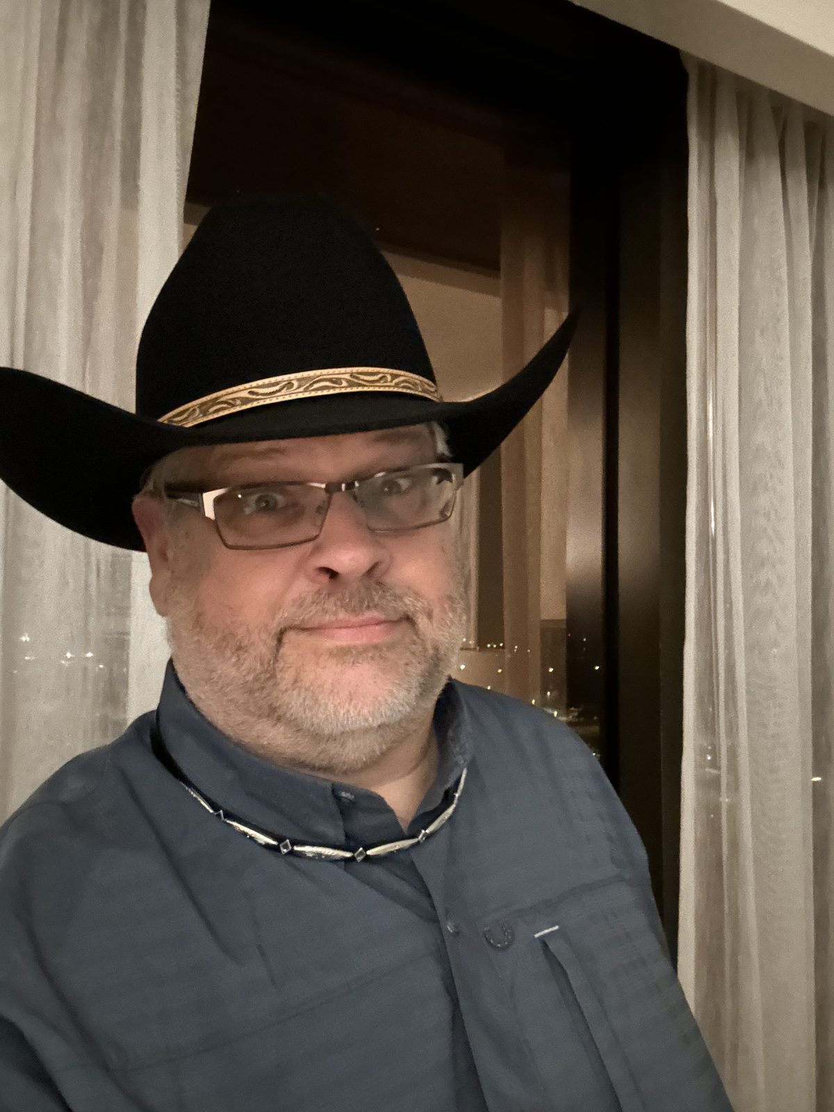Ernie in a black cowboy hat with a patterned band, city lights through the window behind him.