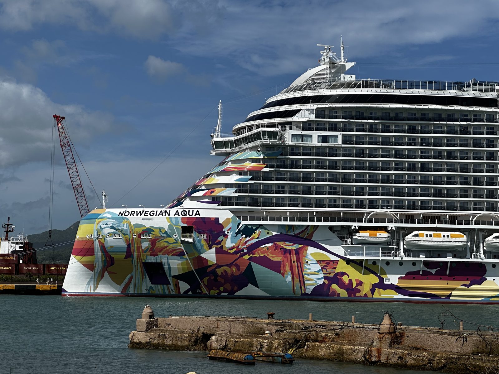 The painted hull of the Norwegian Aqua at Puerto Plata, a crane and a freighter beyond.