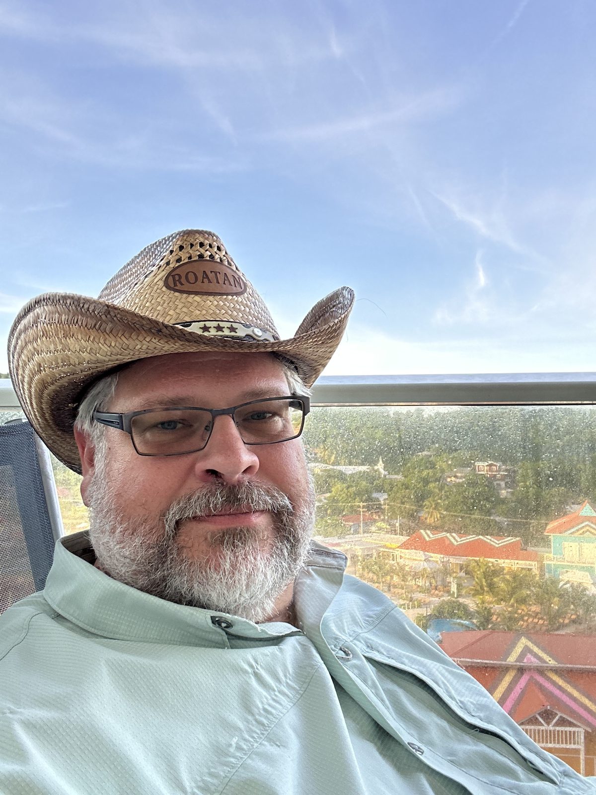 Ernie in the ROATAN hat on a balcony above the painted rooftops of Roatán.