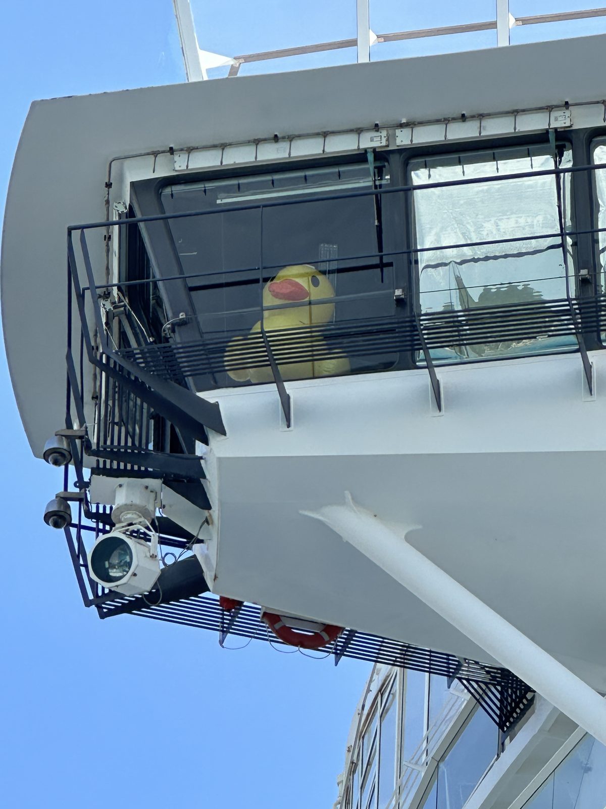 A giant rubber duck riding in the bridge wing of a cruise ship.