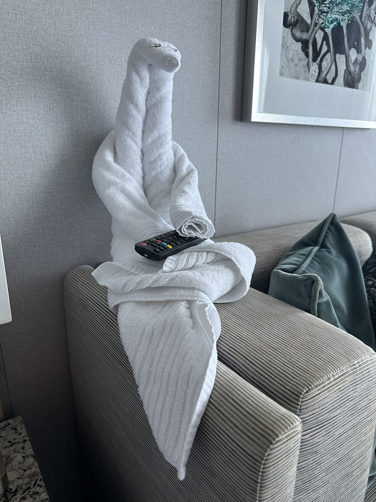A towel animal perched on the arm of a sofa, holding the TV remote.