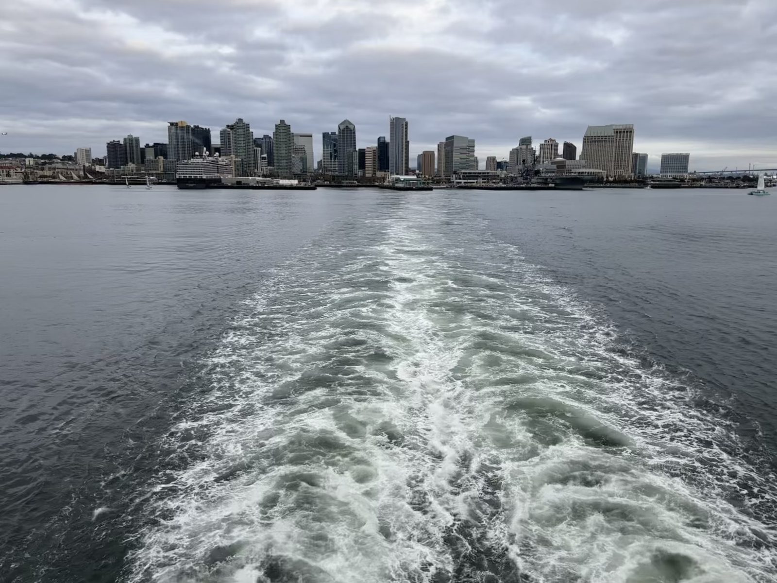 The San Diego skyline receding behind the ship's wake, the USS Midway at the pier.