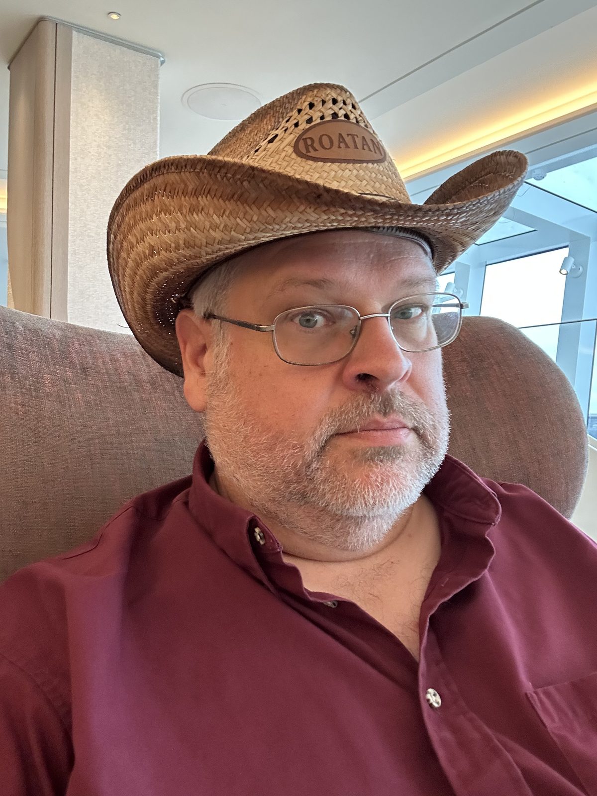 Ernie in a straw hat stamped ROATAN, sitting by a curved window.